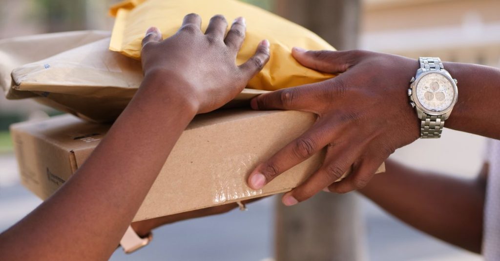 Two individuals exchanging cardboard and padded envelopes, representing delivery services.